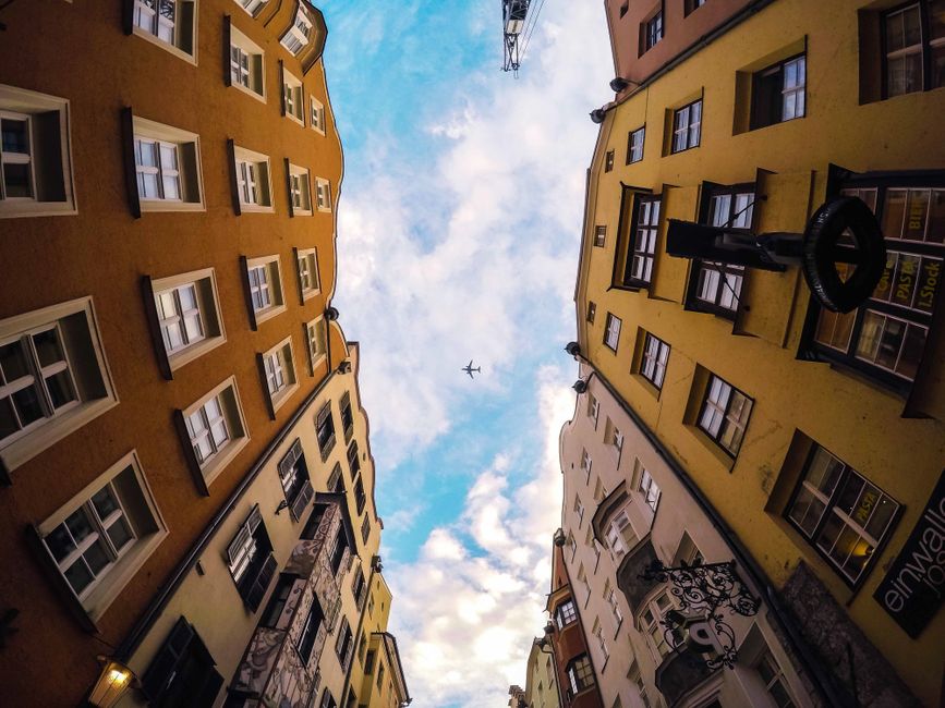 City buildings framing a vivid blue sky with an airplane above, creating dynamic urban scene.